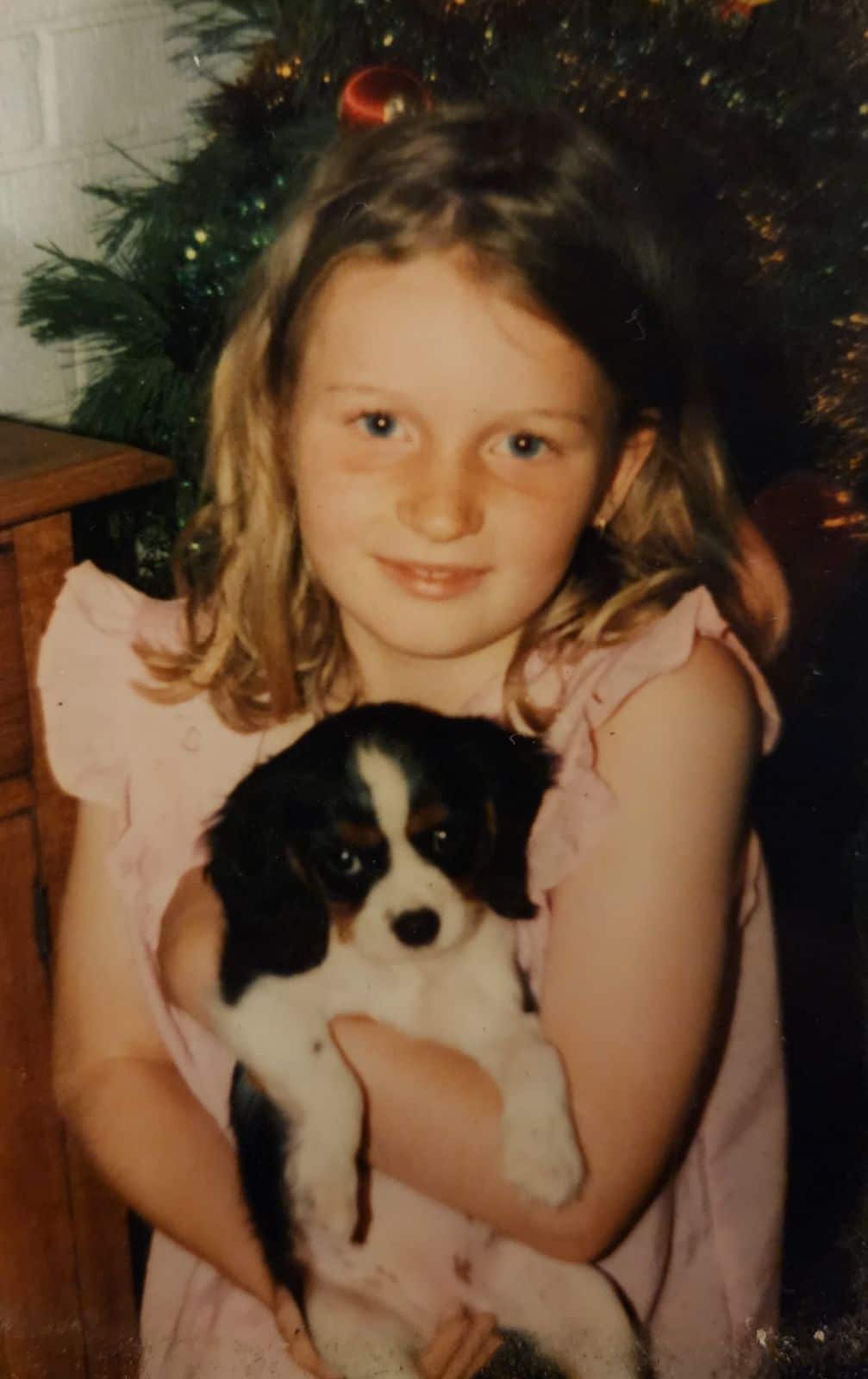 A young girl holding her pet black and white puppy dog, smiling and looking down the camera.