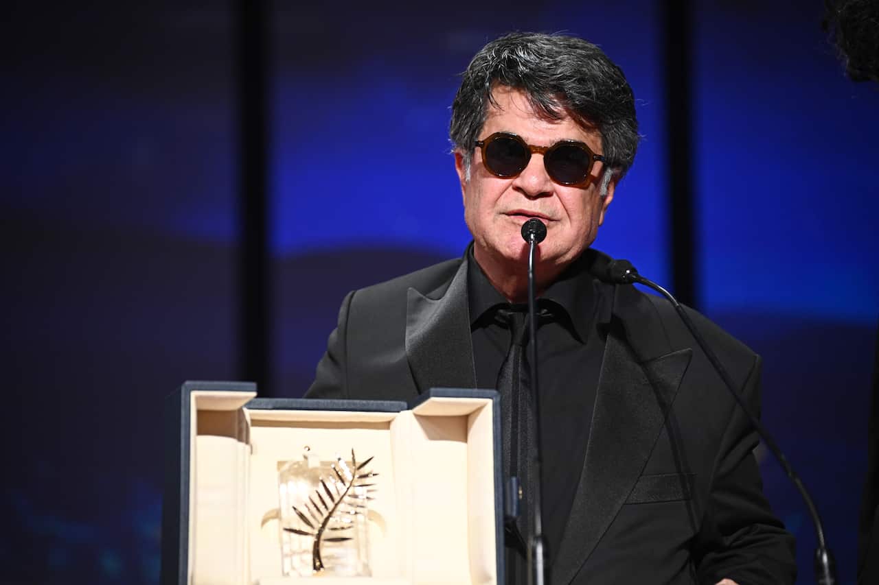 A man wearing an all-black outfit and sunglasses accepts an award on the stage.