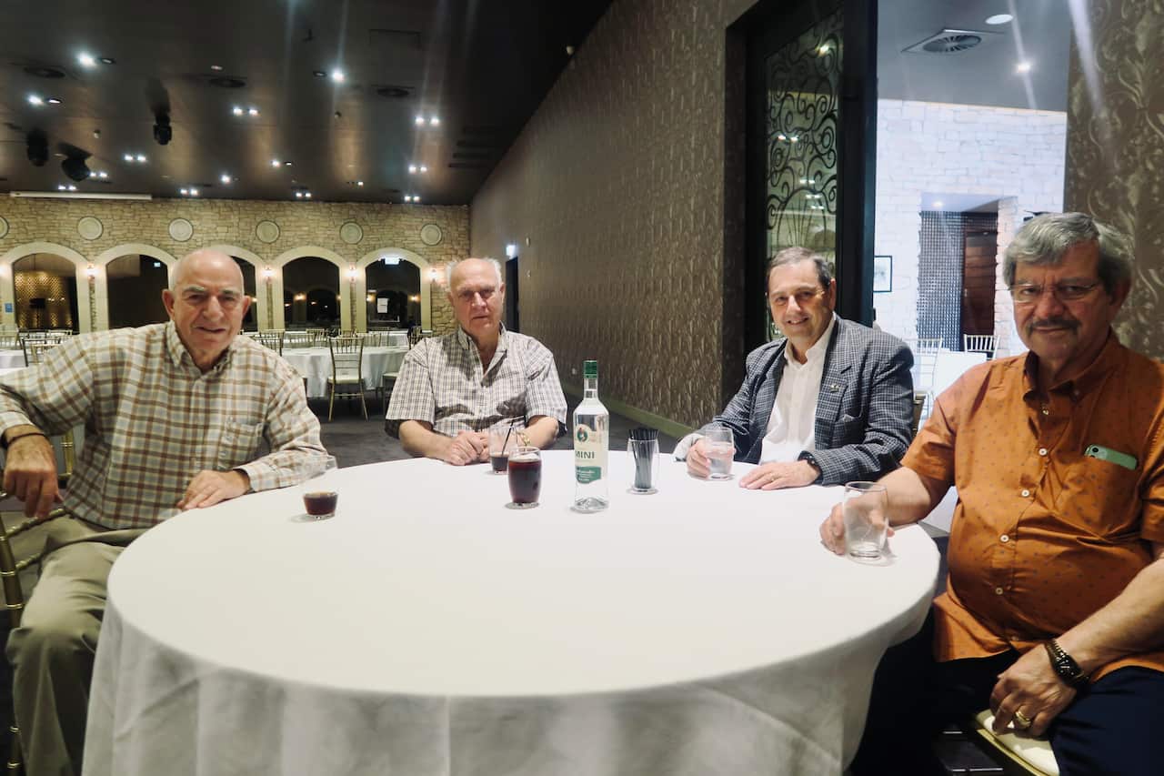 Greek-Australian men sitting at round table looking at camera.
