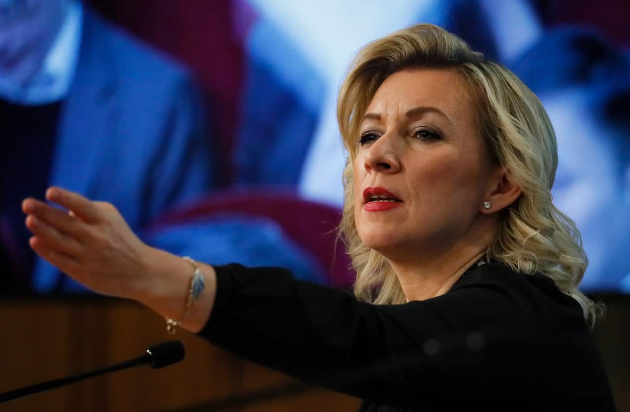 A woman with blonde hair is gesturing with a hand.