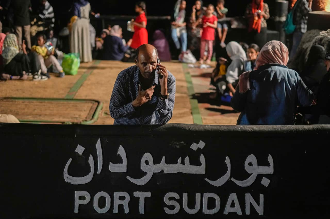 A man standing and leaning on a sign that says "Port Sudan".