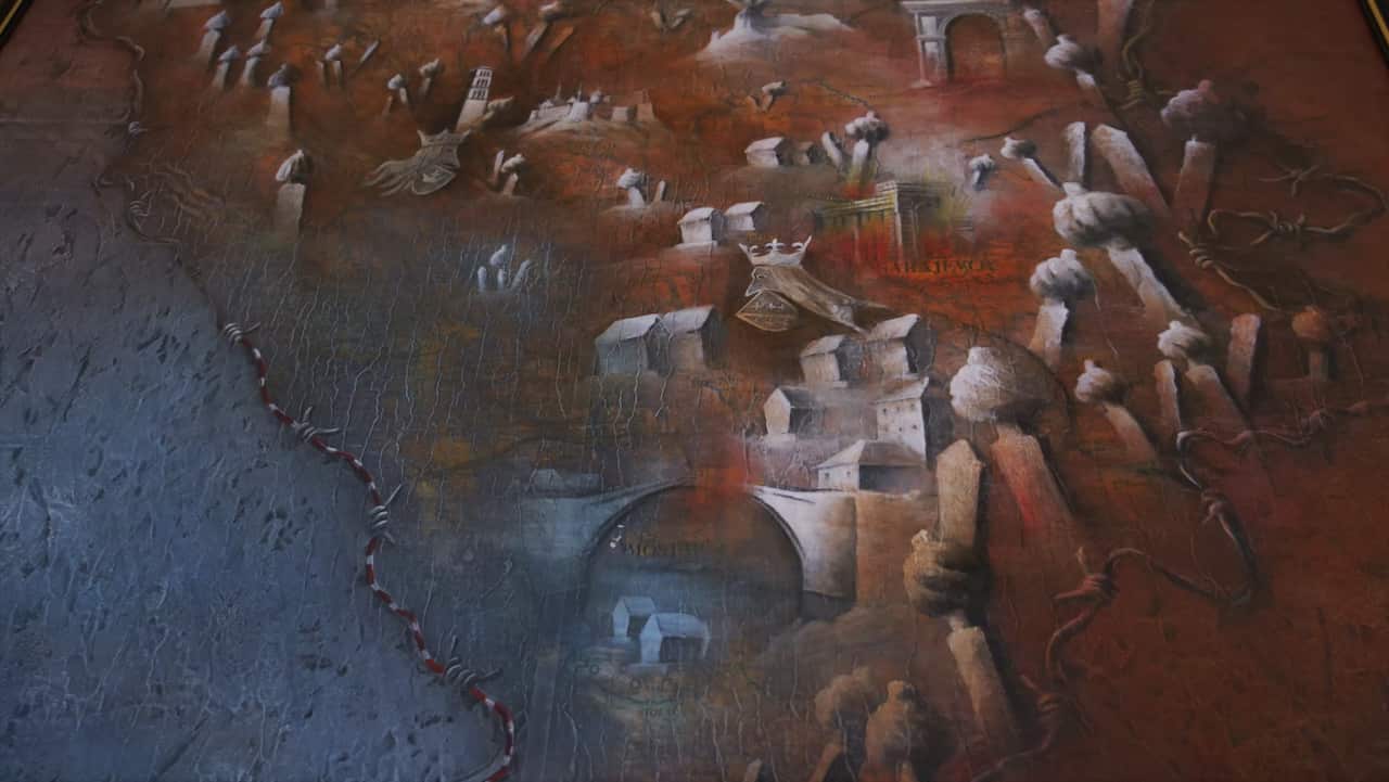 A textured painting depicting a symbolic map of Bosnia and Herzegovina. The artwork includes stylised landmarks clustered around the names of cities. The map is bordered with barbed wire, with smoke plumes and crumbling architecture showing the impacts of war.