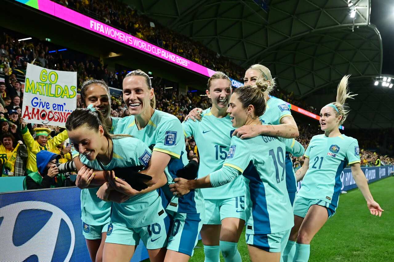 Matildas players cheering and hugging on a stadium field.