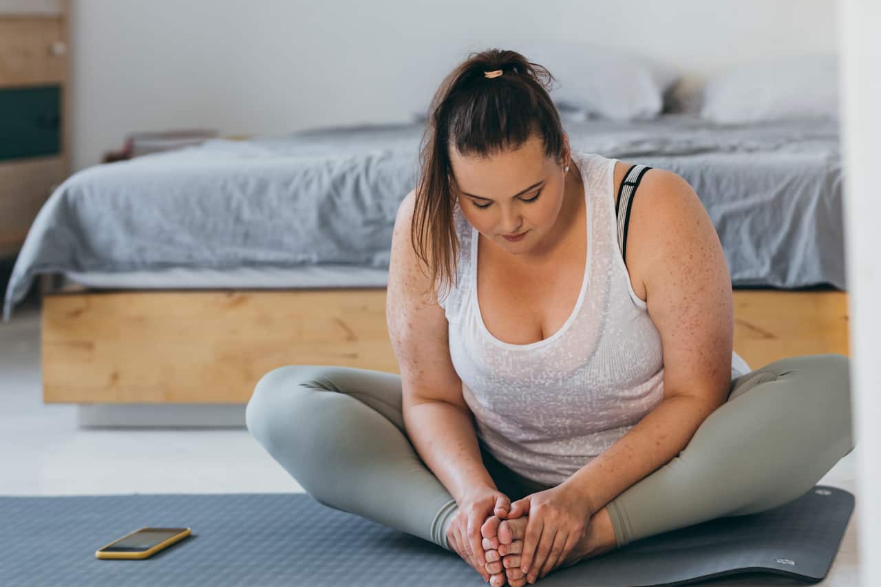 Beautiful plus size woman doing yoga in her bedroom in the morning