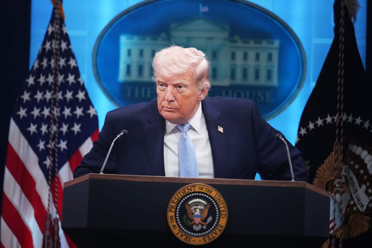 Donald Trump, standing at a podium. American flags and the White House logo are behind him.