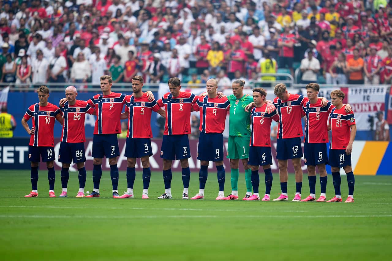 A group of football players in red jerseys stand in a moment of silence with hands over each others shoulders