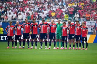 A group of football players in red jerseys stand in a moment of silence with hands over each others shoulders