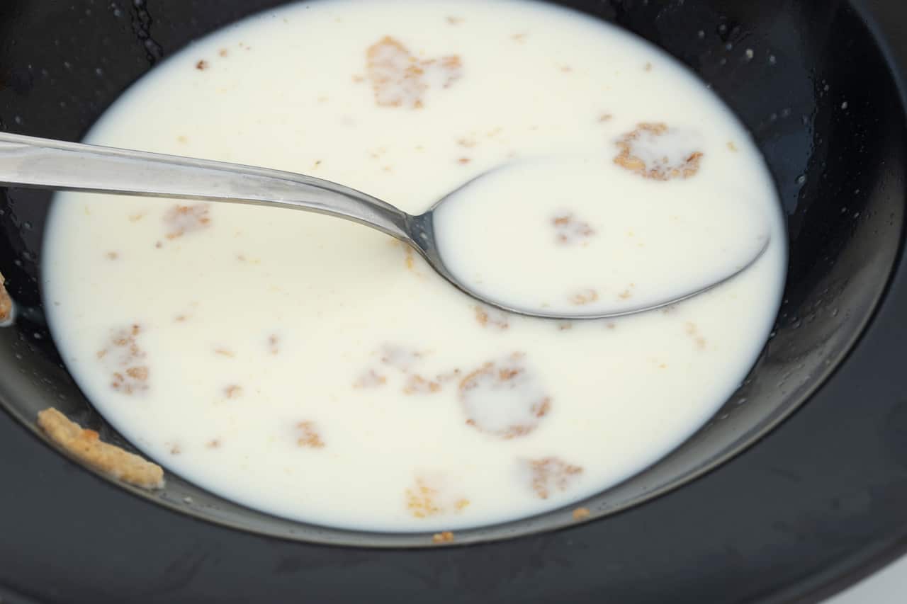 A bowl of milk with some cereal and a spoon in it