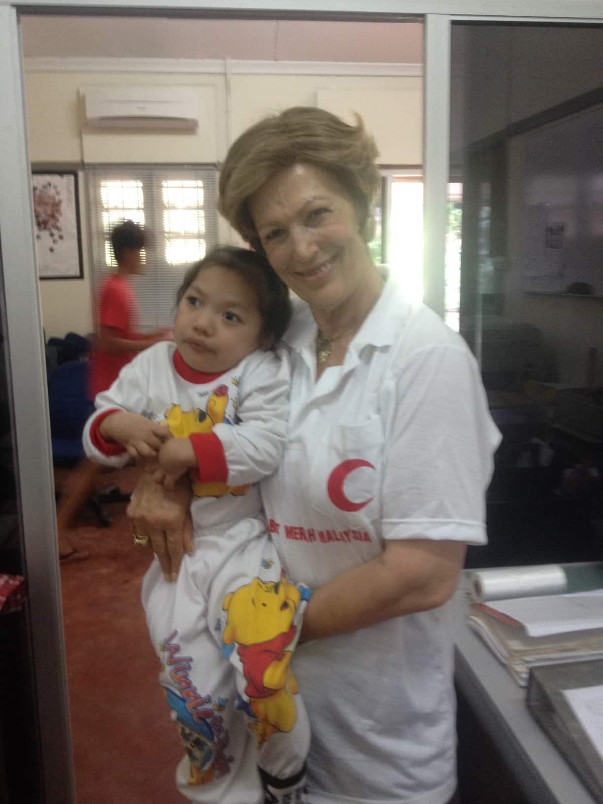 Dimitra volunteering for the Malaysian Red Crescent Society holding a small child