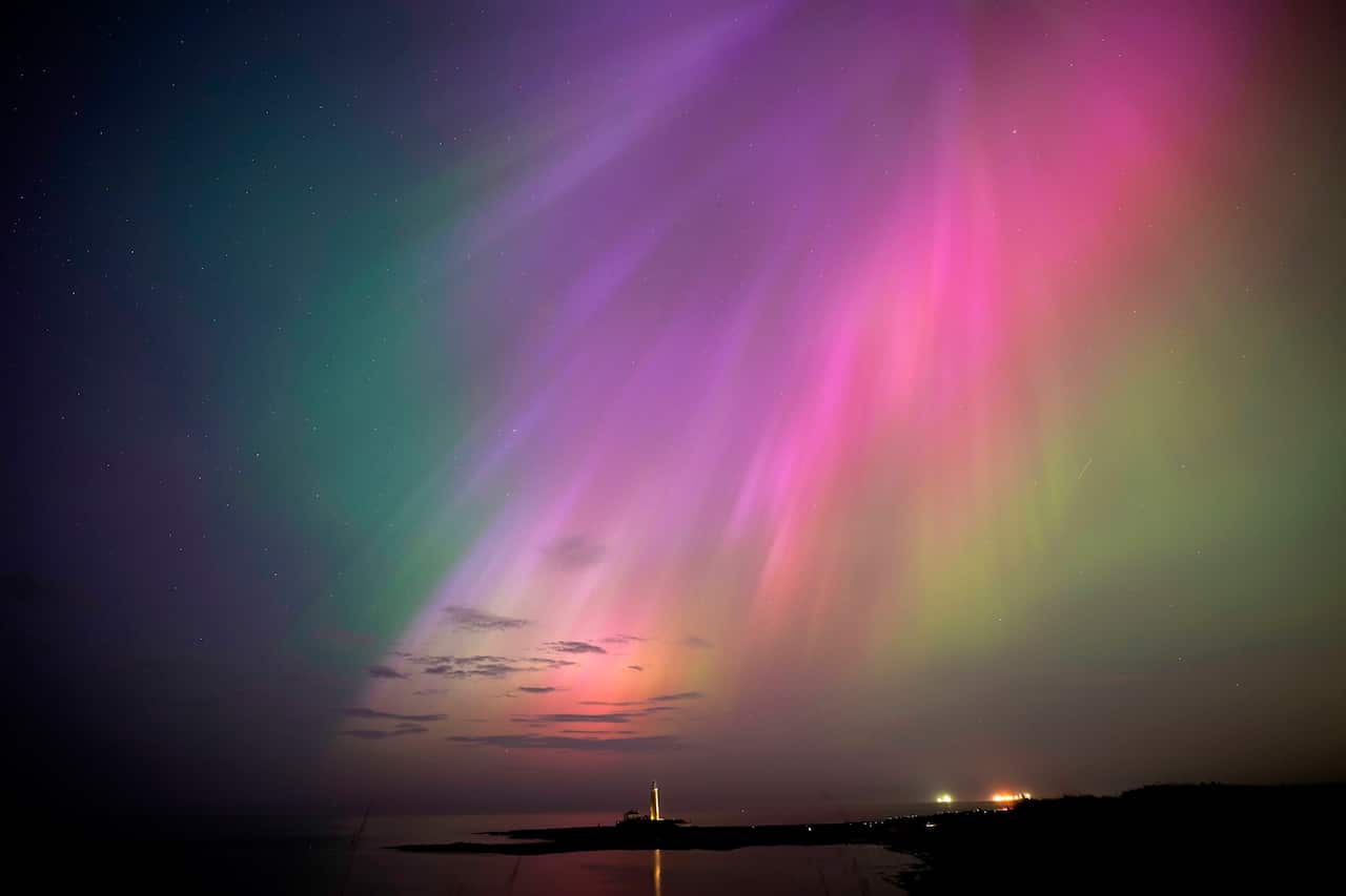 The northern lights glowing above a lighthouse.