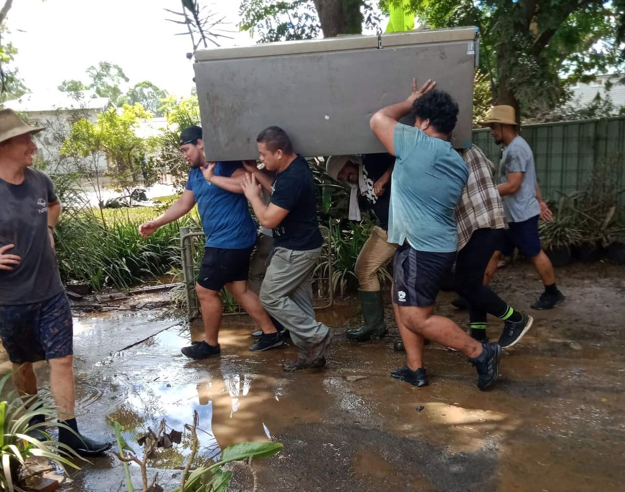 A group of Samoan men work together to help carry heavy items out of homes.