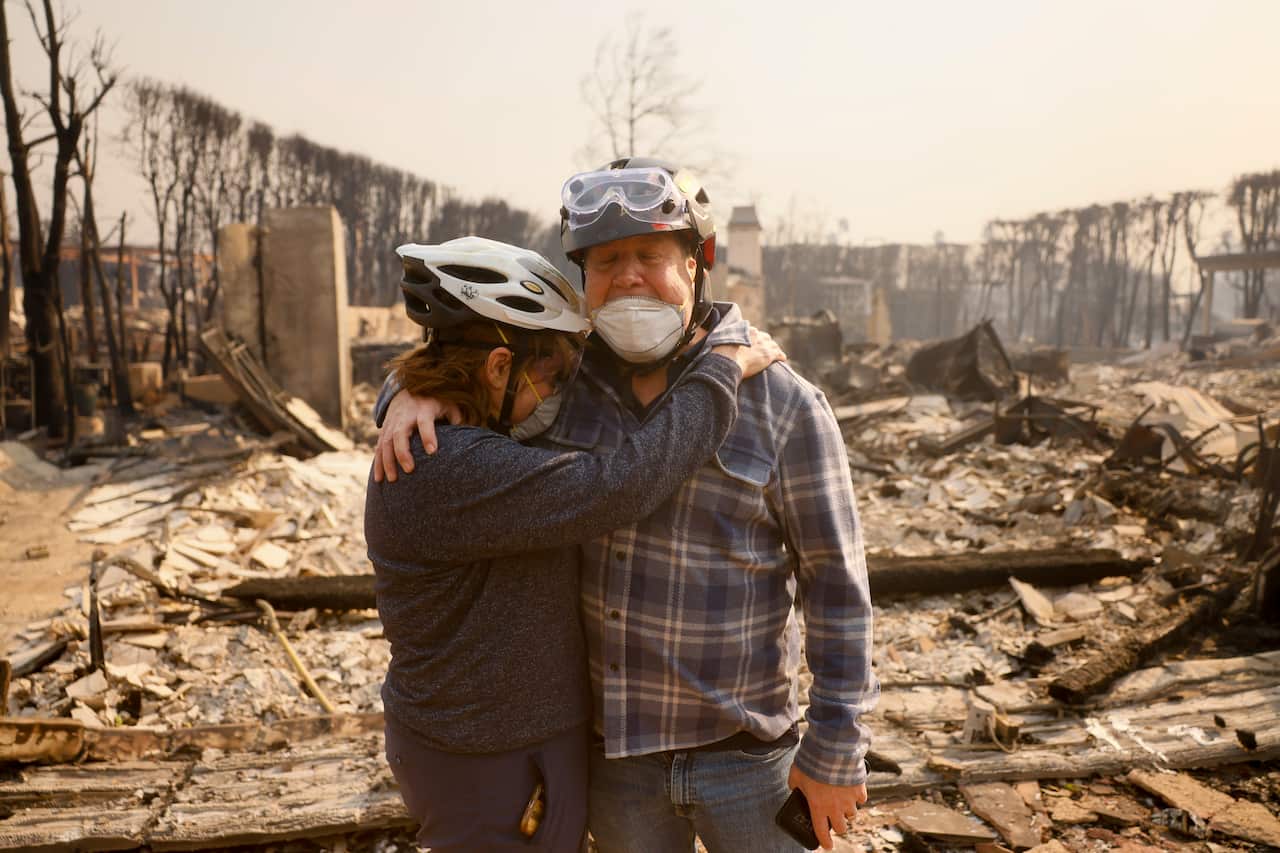 A man and a woman hugging stand amid rubble and buildings destroyed by fire.