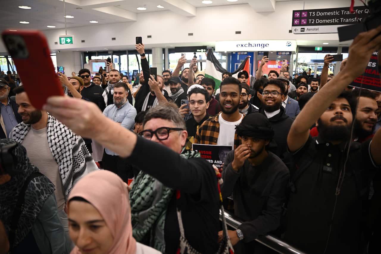 A large crowd of people holding phones and smiling, some holding the Palestinian flag and other signage.
