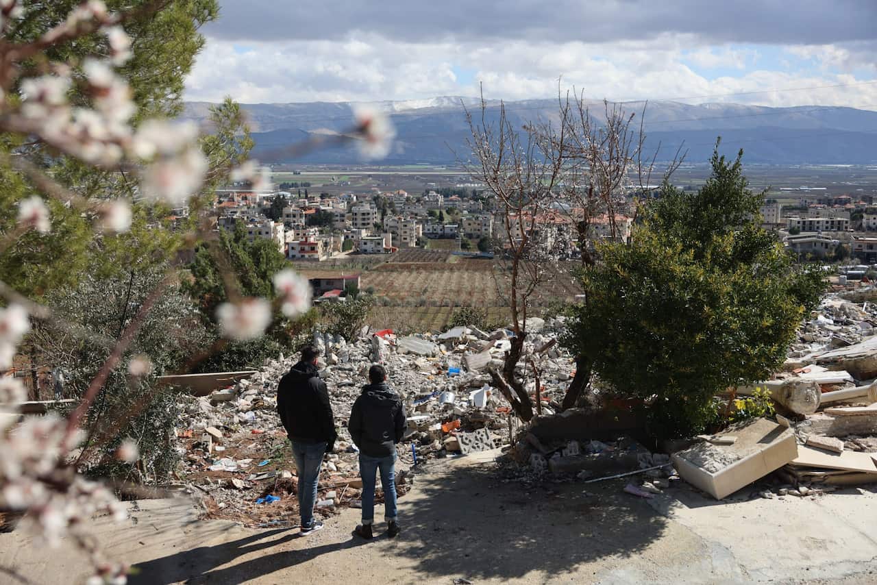Two men stand overlooking rubble at a site of bombardment. town seen in the distance