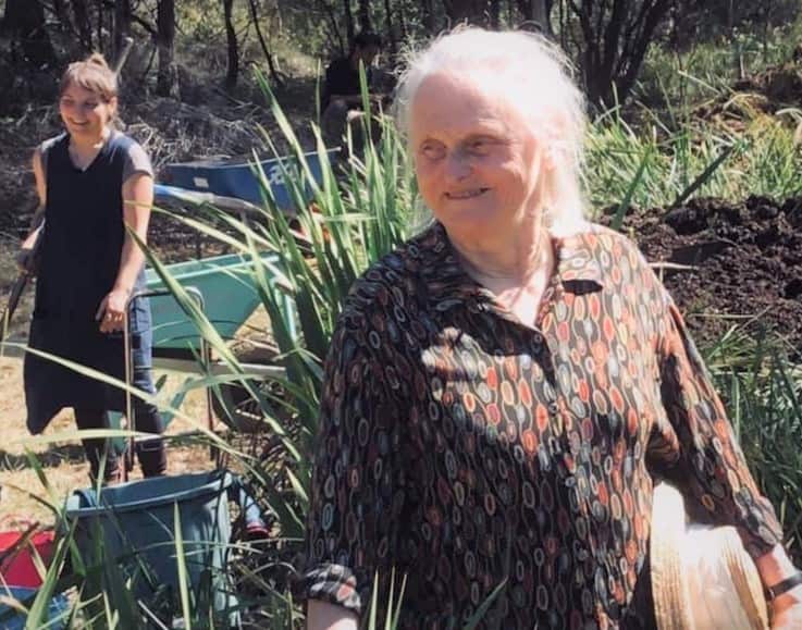 An old woman is standing in her garden with young woman standing behind her.