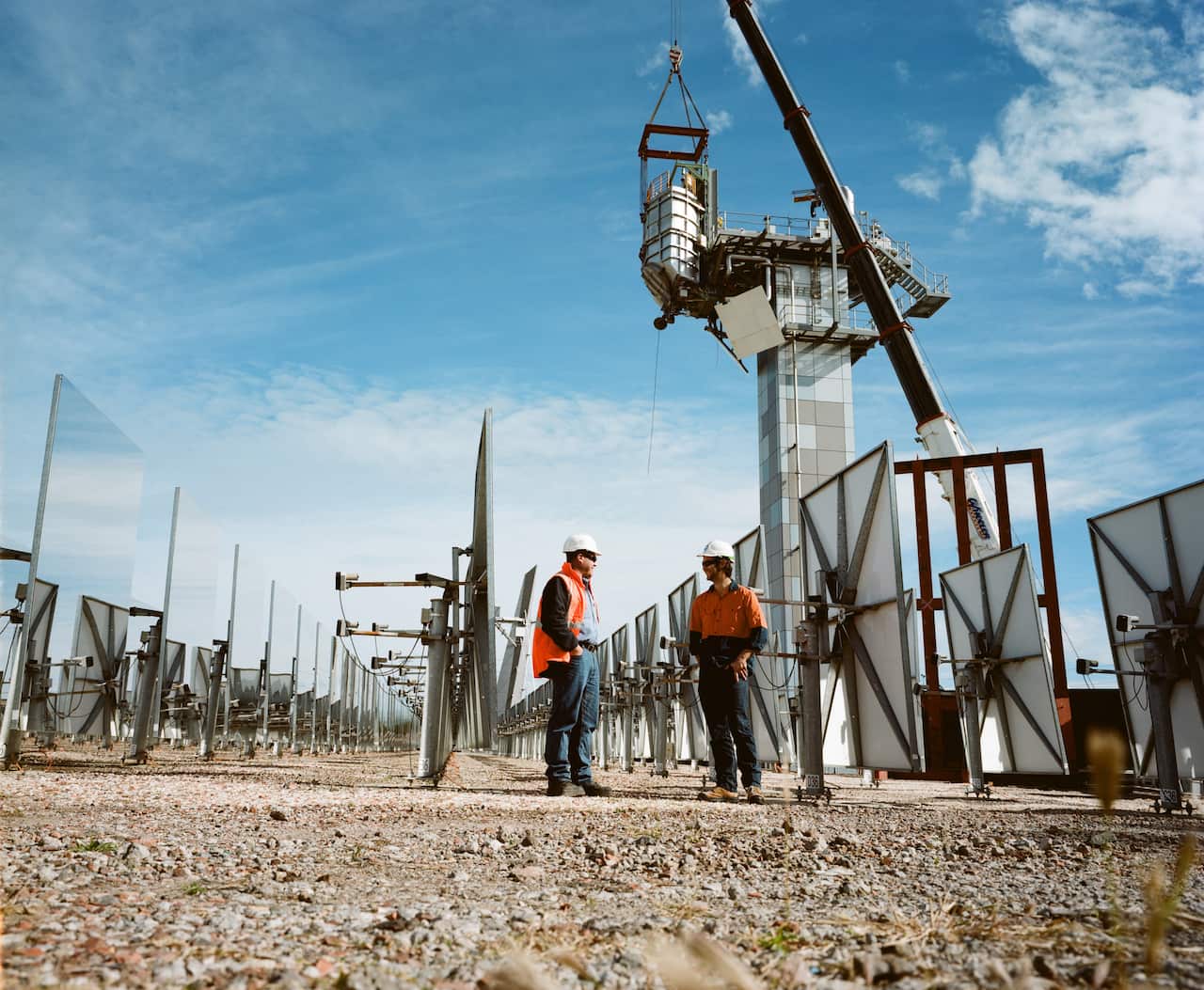 Workers in hi-vis orange vests talk at solar thermal research facility