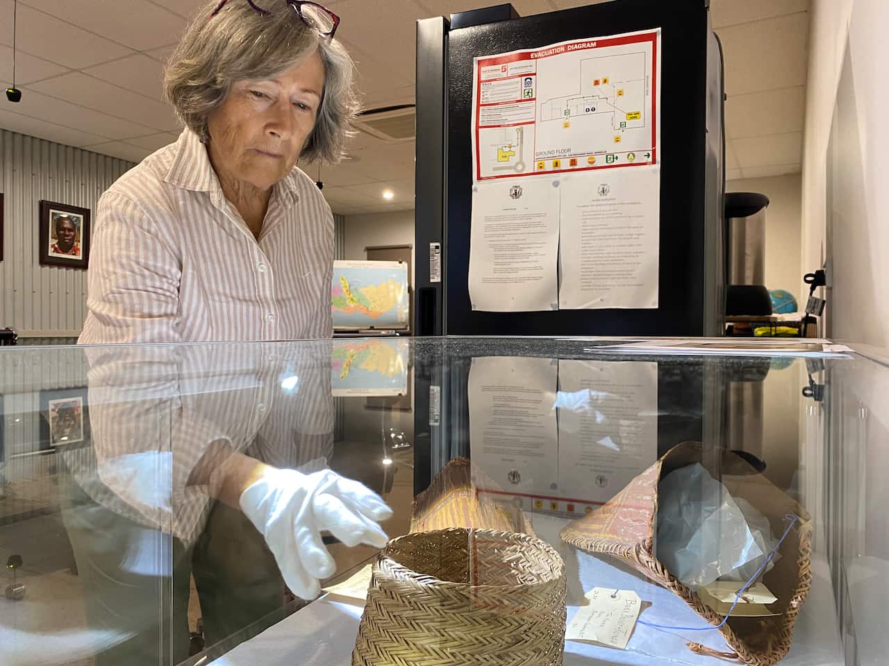 A woman wearing white cloves reaches for a basket in a glass cabinet