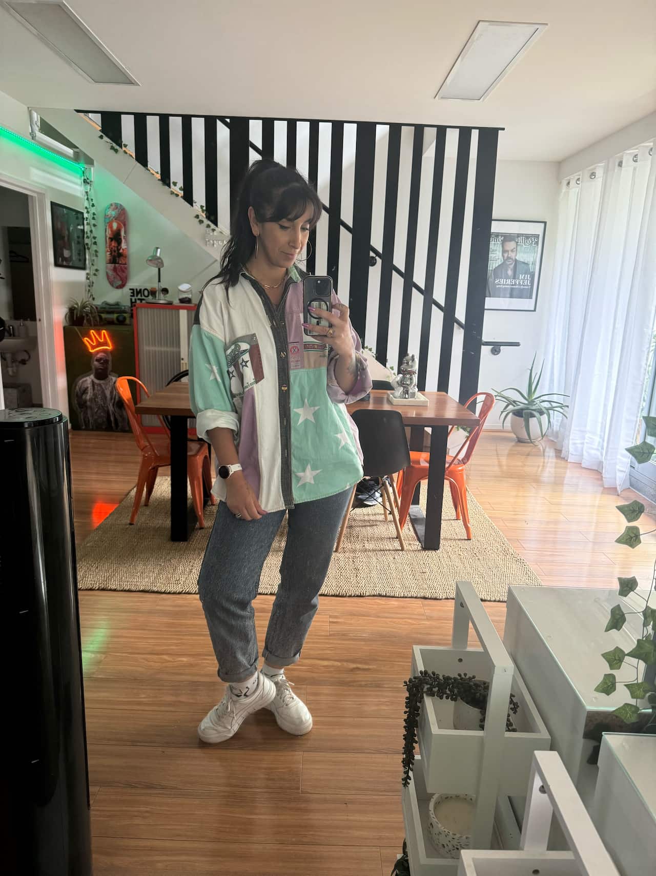 A woman takes a selfie as she stands in her home with a mobile in her hand.