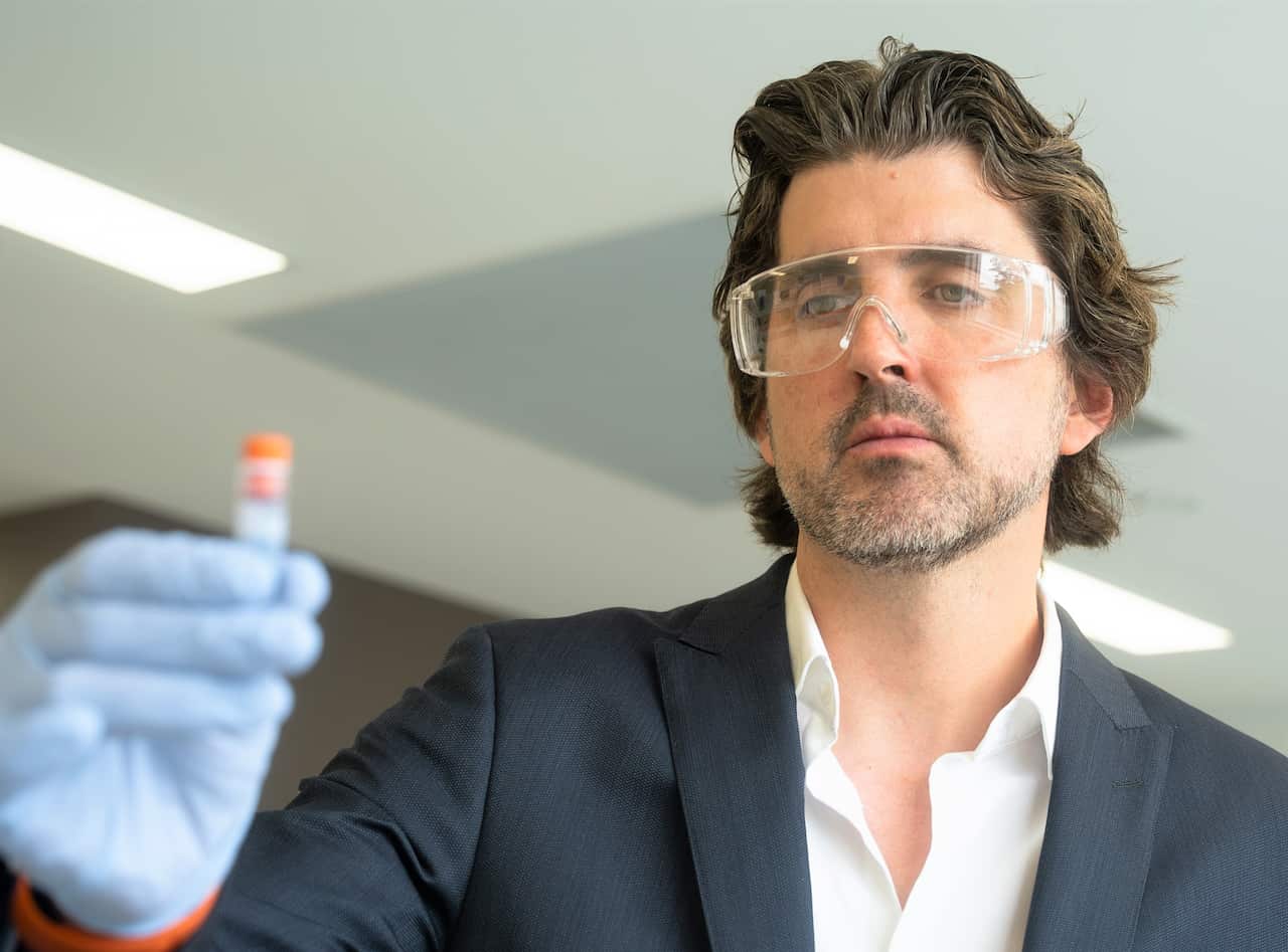 A man in dark suit and white shirt and wearing clear protective goggles looking at a blood sample at ADDRI.