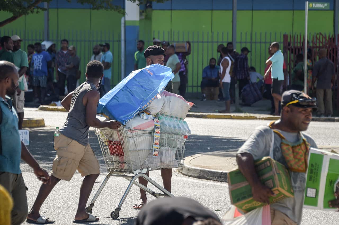People walking along a street holding and wheeling stolen goods.