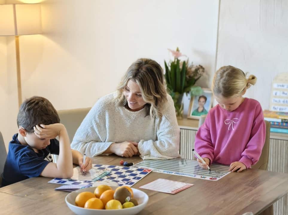 A woman and two young children sit at a table doing schoolwork together.