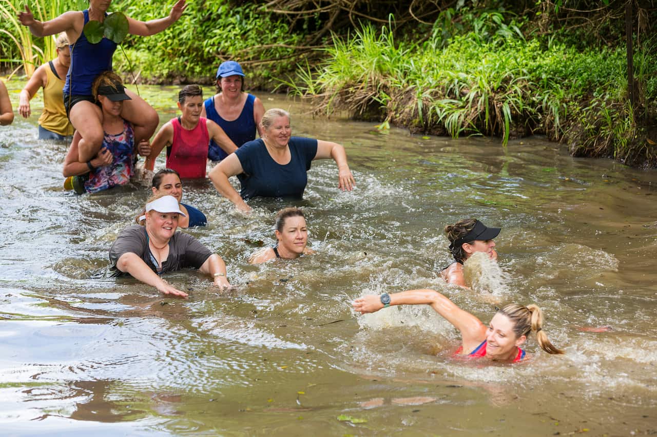 Athletic Mature Women Helping Each Other in a River During an Obstacle Course Mud Run