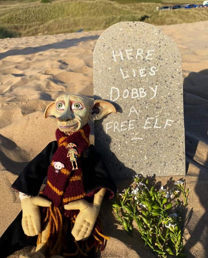 An elf toy resting on a tombstone.