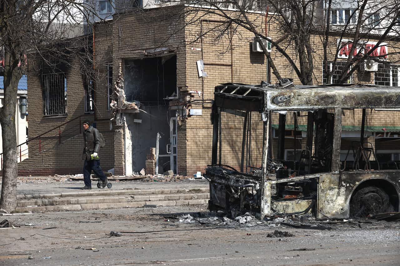 A man walks past the wreckage of a bus.