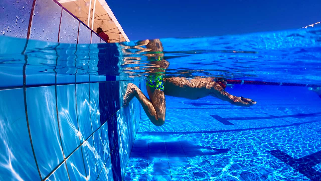 A man kicks off the pool ledge underwater. 