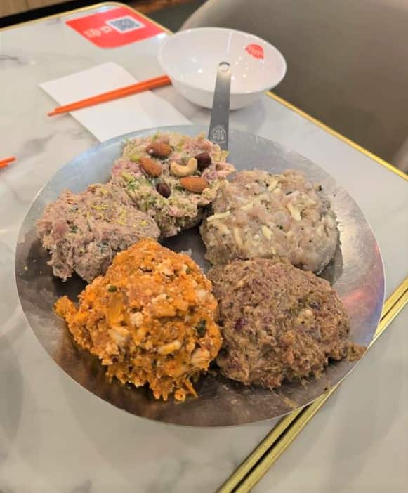 Five dumpling fillings sit on a plate on a table in front of a Chinese-style bowl.