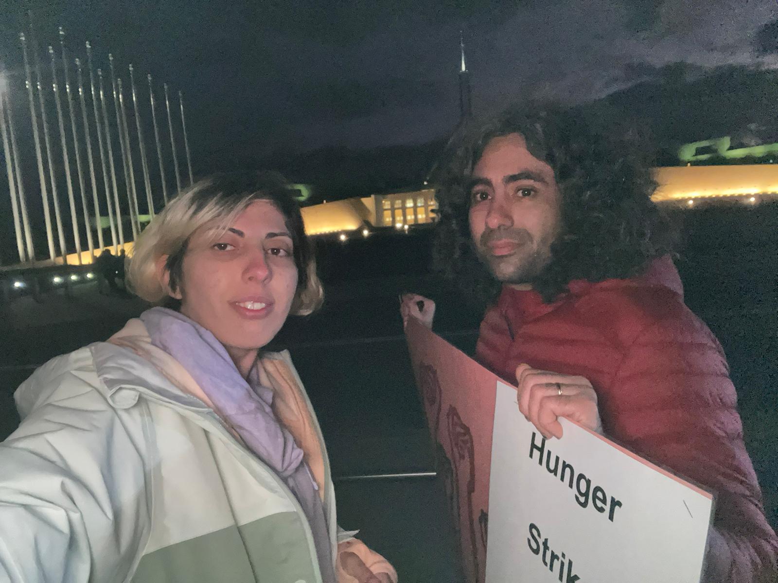A man and a woman outside in darkness in with Parliament House in Canberra in the background