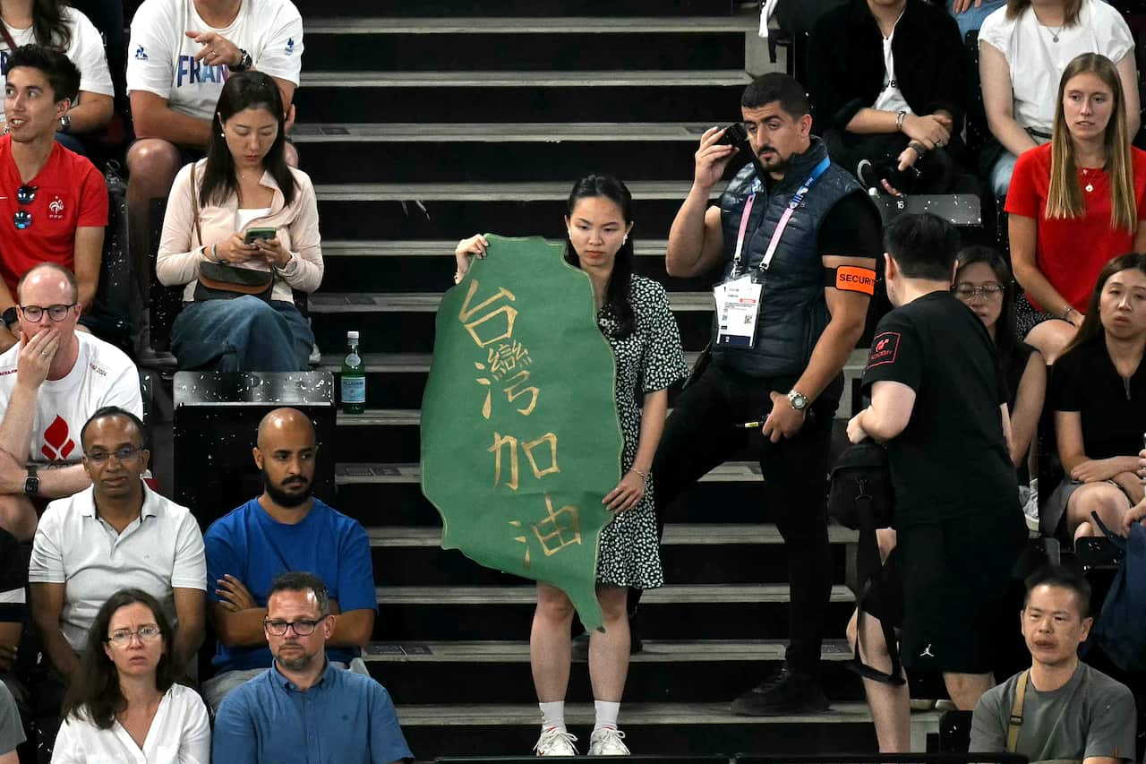 A woman holding a green sign in the shape of Taiwan in the crowd at an Olympic venue in Paris.