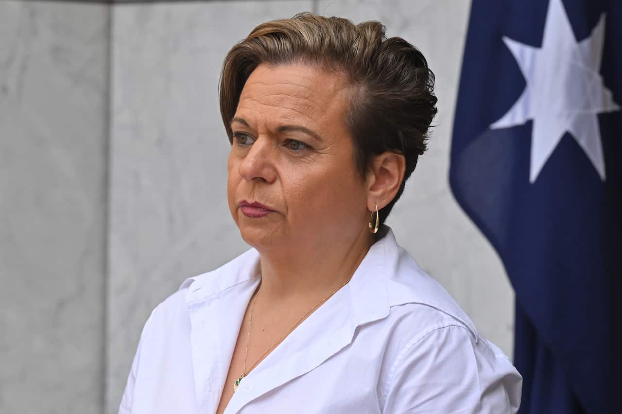 A woman wearing a white button-up shirt with an Australian flag in the background.