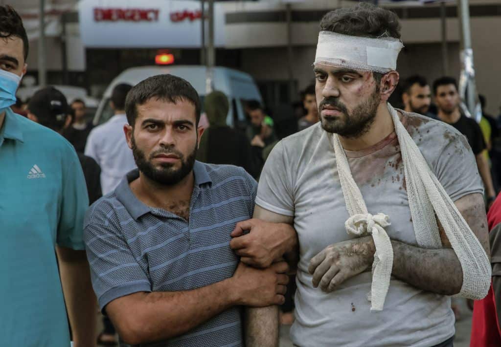 A man helps an injured man with his arm in a sling.