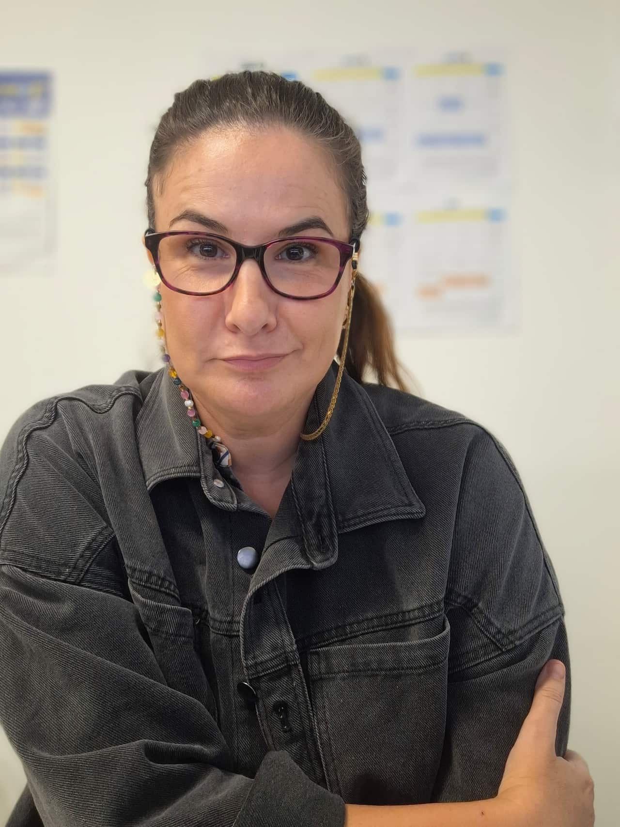 A woman with dark hair and glasses looks at the camera with a neutral expression on her face.