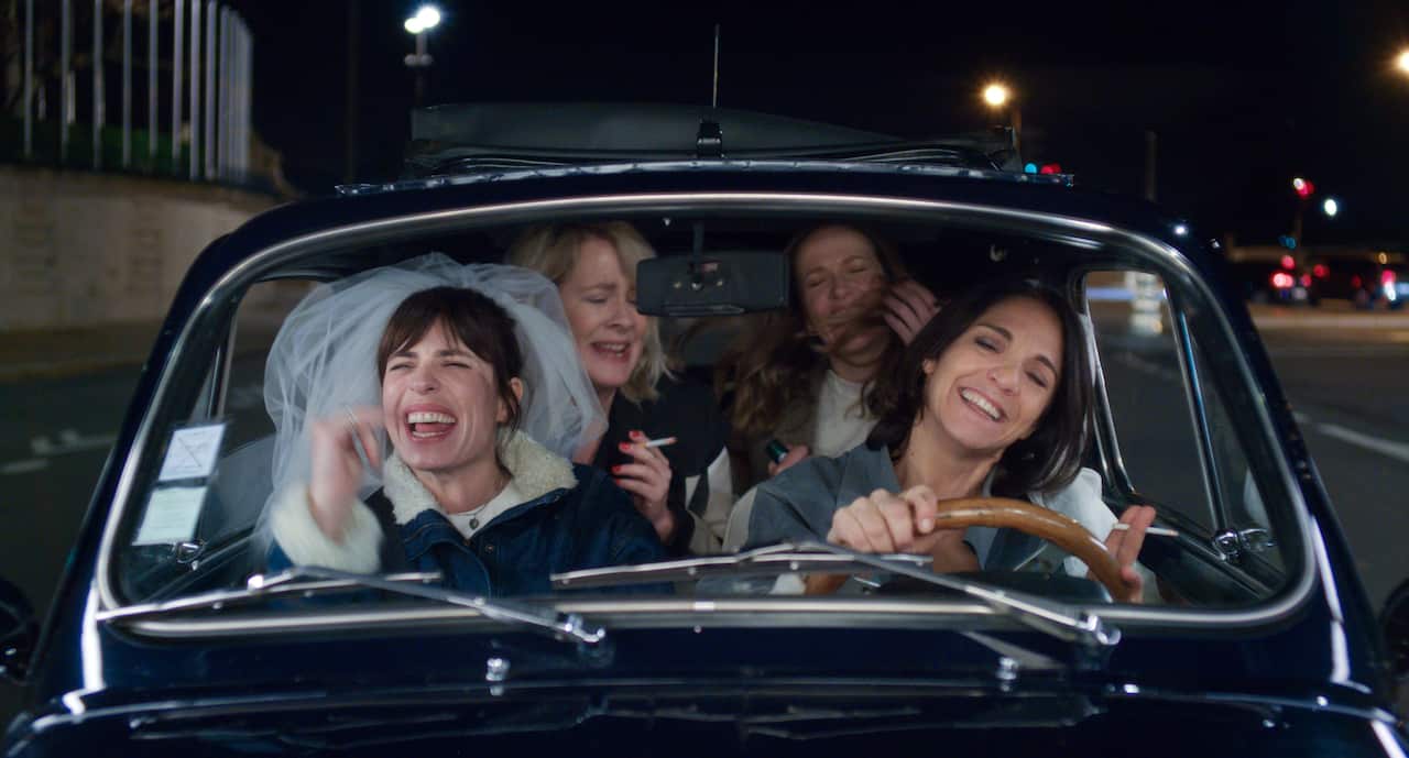 Four women crammed into a Mini car are laughing and having fun in French series Shambles