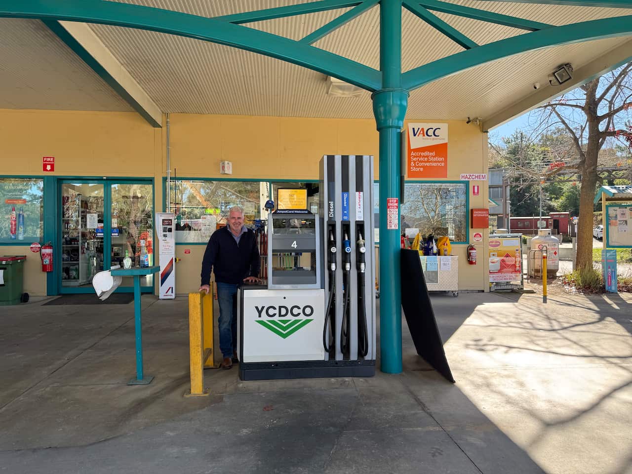 A man in a black jumper stands outside a fuel station.