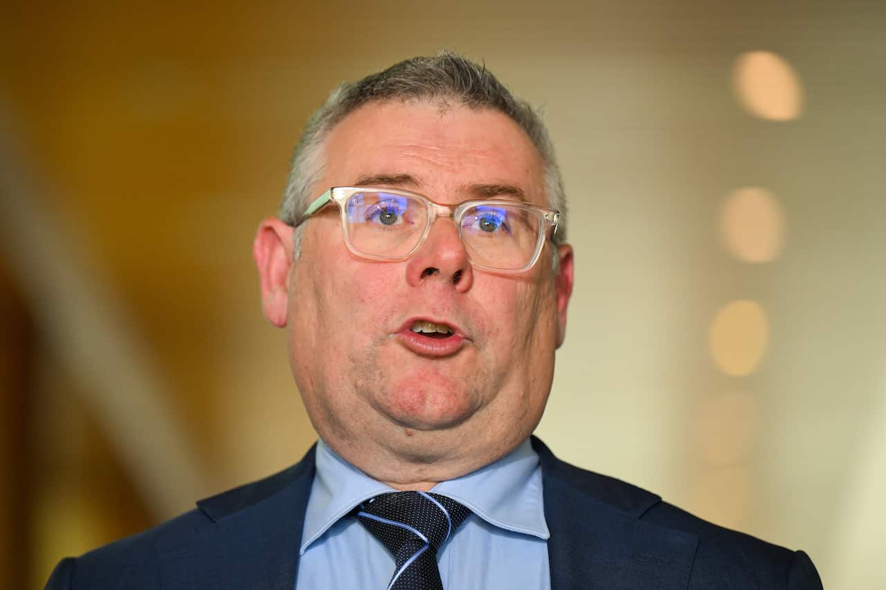 A man earing clear framed glasses and a blue suit, shirt, and tie