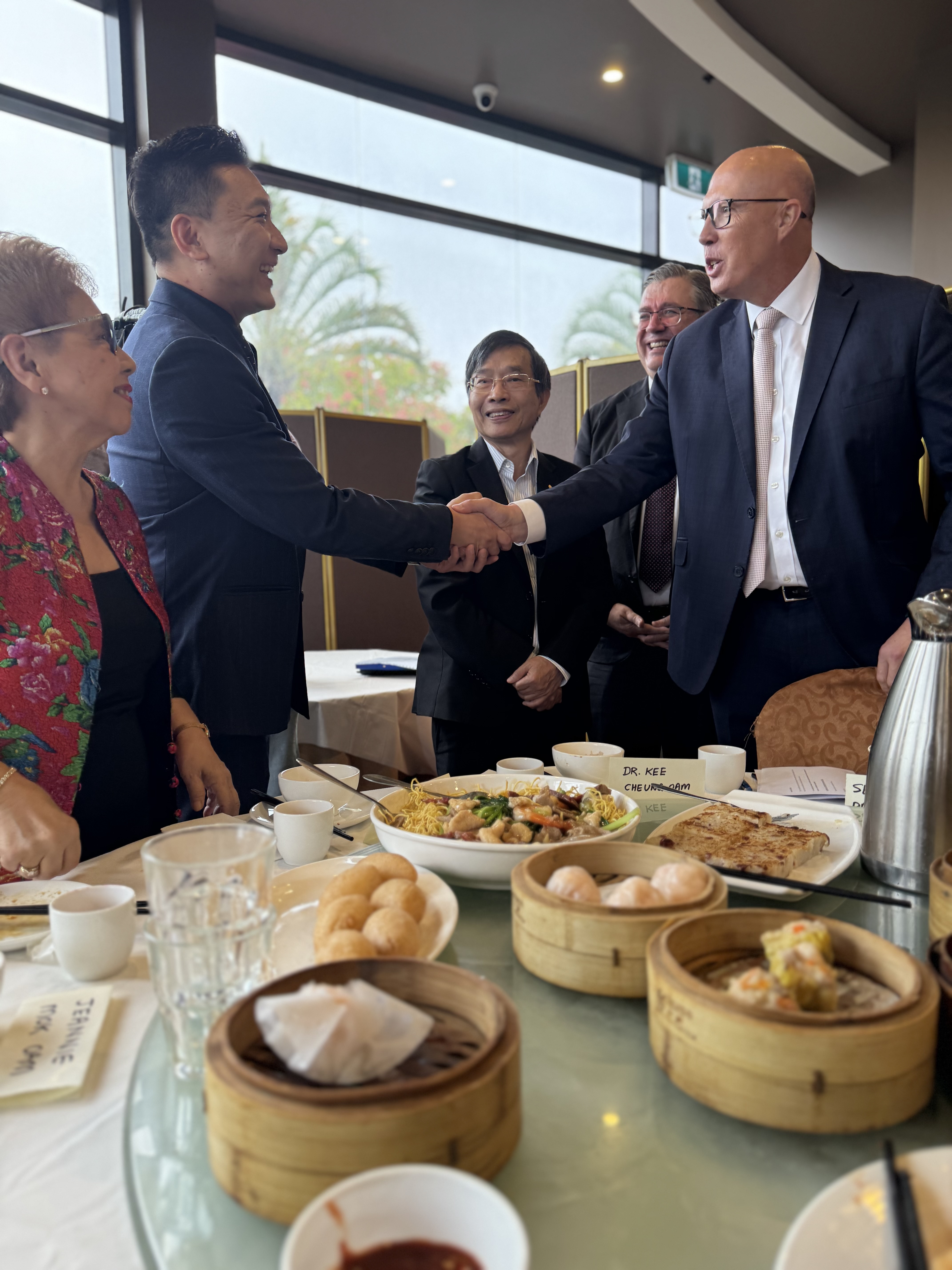 Peter Dutton shakes hands with a man while standing next to a table of yum cha dishes. 