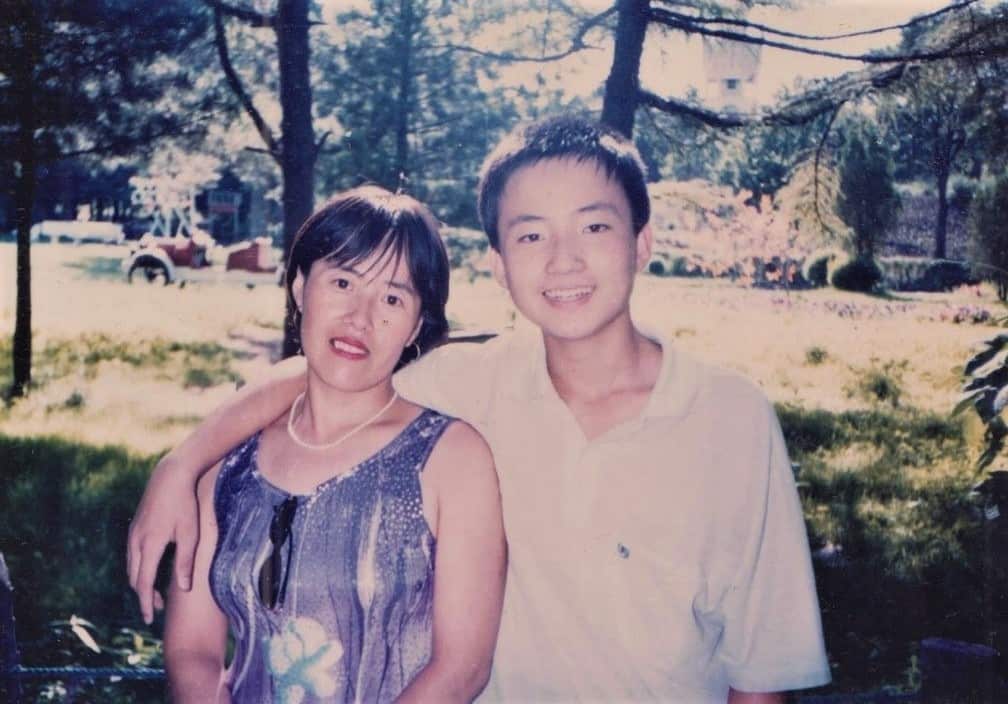 A man stands near a park with his arm around a woman's shoulder.