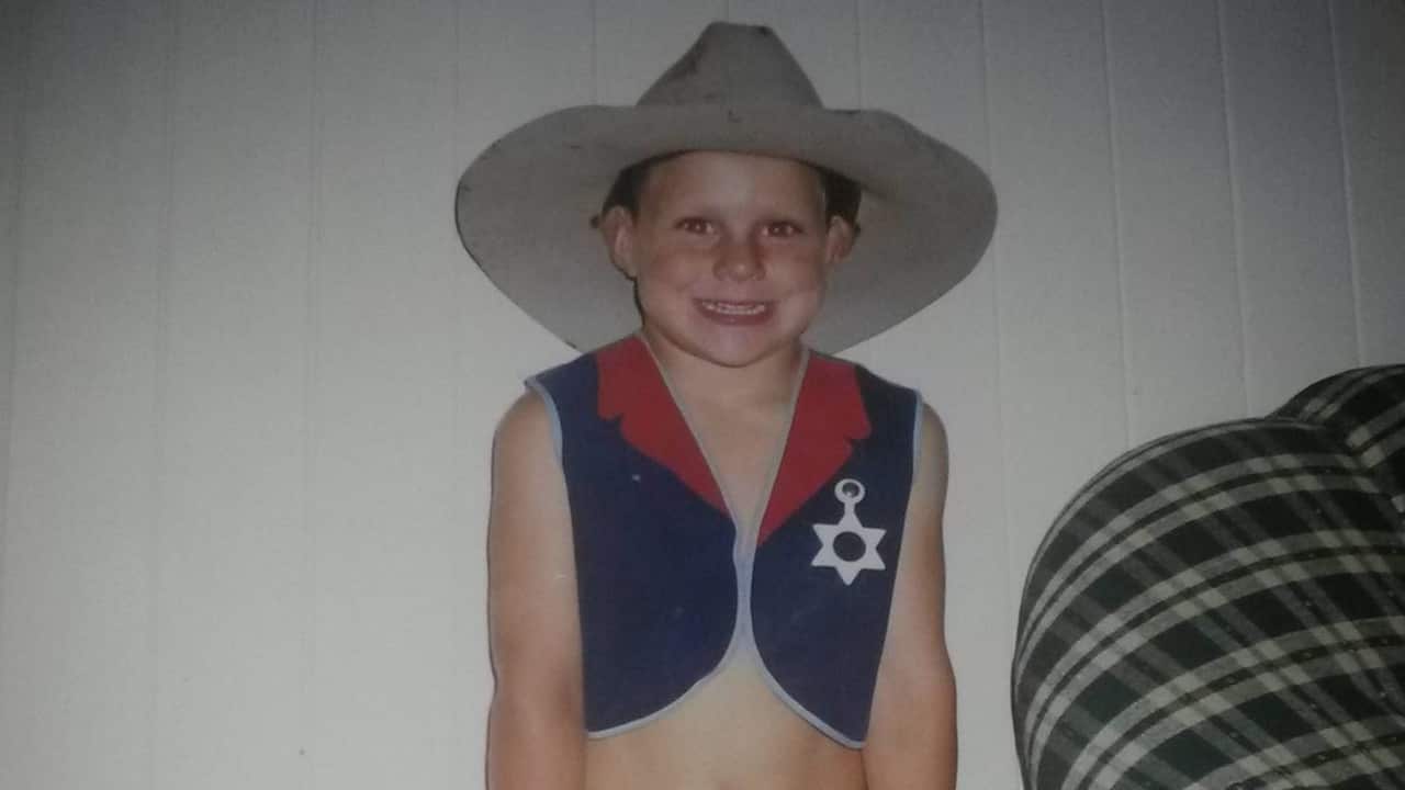 a young boy dressed in a cowboy outfit smiles at the camera in front of a white wall