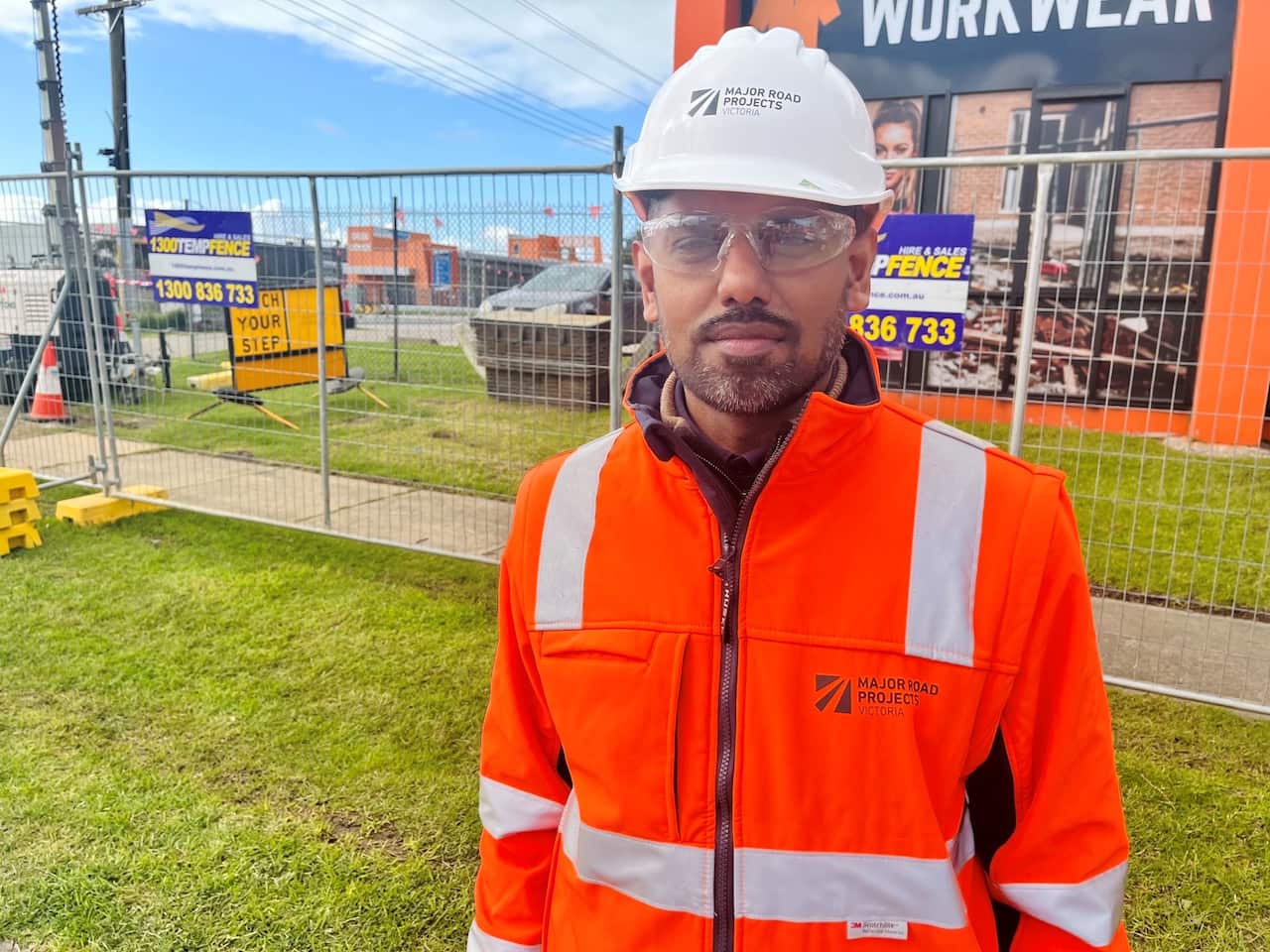 A man wearing an orange hi-vis jacket, clear safety goggles and a white hard hat