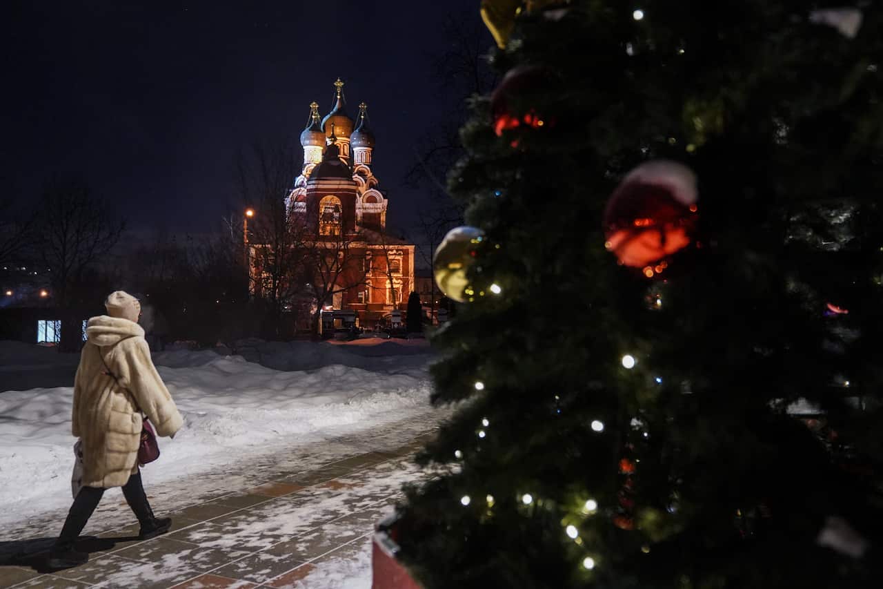 A woman dressed in winter clothing walks past an Orthodox church with a Christmas tree on her right.
