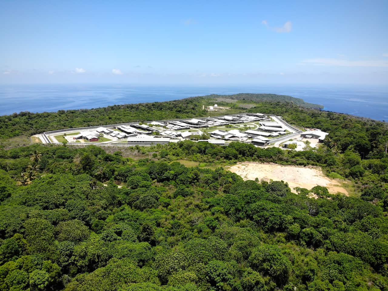 Aerial view of immigration detention centre surrounded by trees and the ocean.