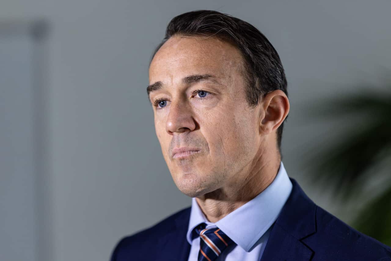 A man in a dark blue suit and light blue shirt staring to the left of the camera.