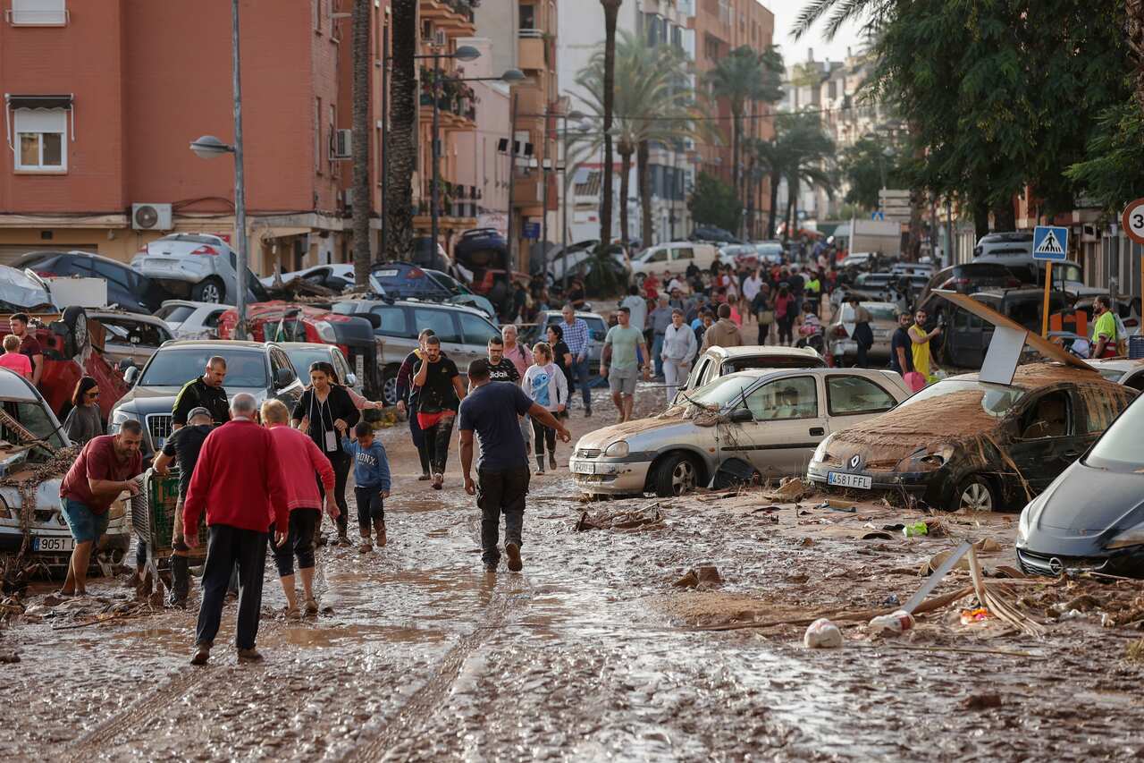 A group of people move between wrecked cars in thick mud.