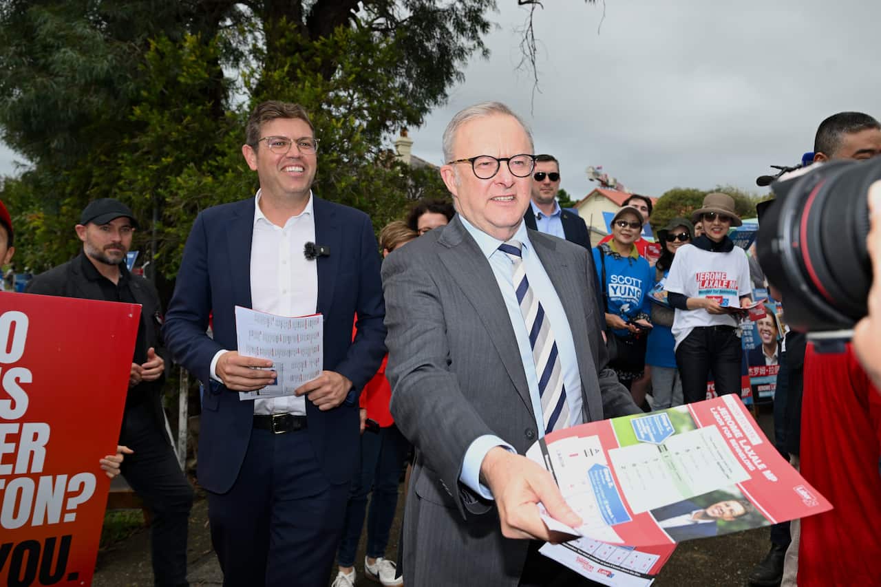 Wearing a grey suit, Anthony Albanese hands out red Labor how-to-vote cards at an early polling booth.