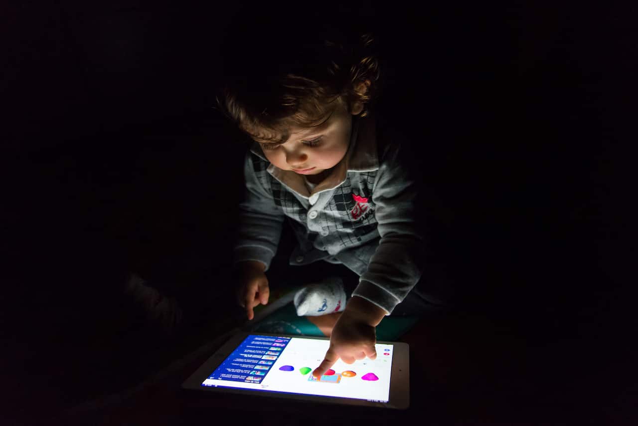 A child in a dark room playing on an iPad.