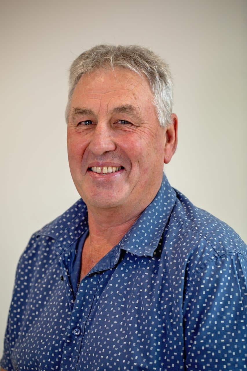 A headshot of Mark Mudie in a blue shirt