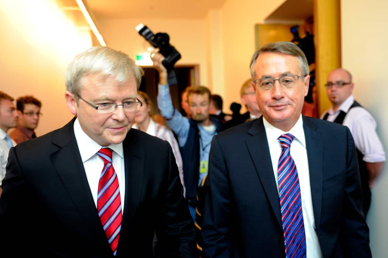 Two men wearing suits are walking in front of the media personnel inside a corridor.